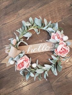 a wreath with the word hello written on it and some pink flowers in front of it