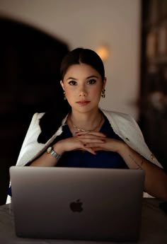 a woman sitting in front of a laptop computer with her hands on her chest and looking at the camera