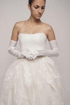 a woman wearing white gloves and a wedding dress with flowers on it's waist