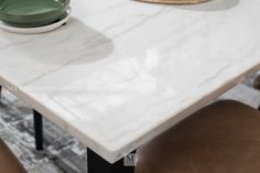 a white marble dining table with two brown chairs and a bowl on the table top