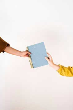 a woman holding a notebook in her hand and handing it to another person's hand