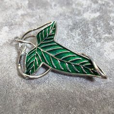 This beautiful piece symbolizes the spirit and bond of those entrusted to save Middle-Earth. Worn by Frodo, Legolas, Aragorn, Boromir, and the other the members of the Fellowship. Sterling Silver and copper with green enameling 2.75 inches by 2 inches Pin back closure Includes chain and can be worn as necklace Tag us on IG 📸 @CargoHoldDesigns and use #cargoholddesigns with a selfie of you and your product to be featured on our page and website! Feel free to contact us if you have any questions Leaves Of Lorien, Aragorn Costume, Legolas Aragorn, The Two Towers, Fellowship Of The Ring, Replica Prop, Legolas, Movie Props, Middle Earth