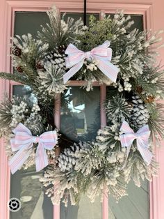 a wreath with pink and white bows hanging on the front door, decorated with pine cones