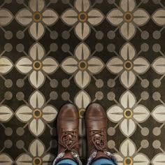 a pair of brown shoes sitting on top of a floor next to a patterned wall