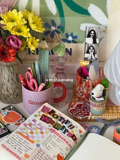 an open book sitting on top of a table next to flowers and other office supplies