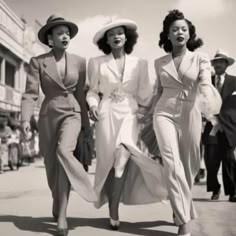 three women in suits and hats walking down the street