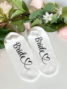 two white socks with the words bride and groom written on them next to some flowers