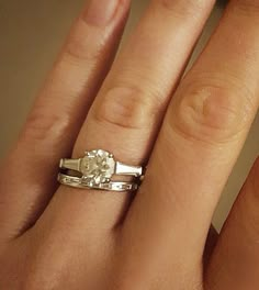 a woman's hand with two wedding rings on top of her finger and the other hand holding an engagement ring