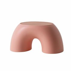 the pink stool is shaped like an arch, and sits on top of a white surface