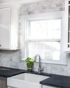 a kitchen with marble counter tops and white cabinets, along with a window over the sink