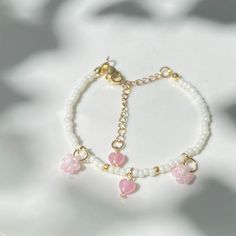 a white bracelet with pink hearts on it and gold chain hanging from the clasps