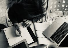 a woman sitting at a table with her laptop and notebook in front of her, writing