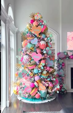 a brightly colored christmas tree with lots of hearts on it's top and decorations around the base