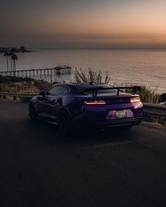 a purple sports car is parked on the side of the road by the ocean at sunset