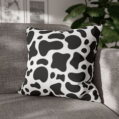 a black and white pillow sitting on top of a couch next to a potted plant