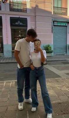 a man and woman taking a selfie in front of a pink building on the street