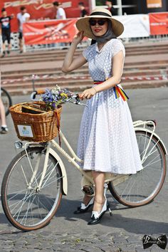 a woman in a dress and hat is standing next to a bicycle with a basket