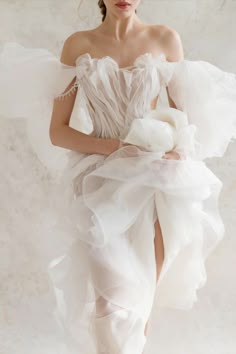 a woman in a white dress with ruffles on her skirt and heels, posing for the camera