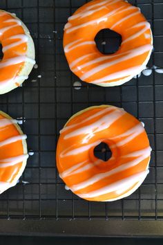 four glazed donuts with orange and white icing on a cooling rack, ready to be eaten