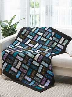 a couch with a blue and black quilt on it next to a white chair in front of a window