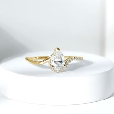 a white and gold ring sitting on top of a white stand with a diamond in the middle