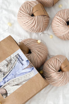 four balls of pink yarn sitting on top of a white blanket next to a brown box