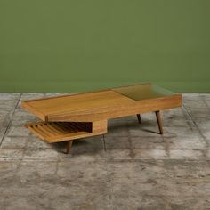 a coffee table with an open drawer on the bottom and one shelf below it, against a green wall