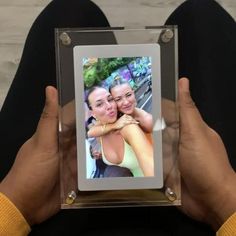 a person holding up a glass frame with a picture of two women in the background