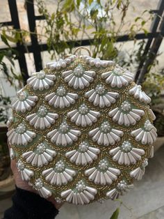 This is a beautiful handcrafted clutch bag made with love.It has intricate handwork which showcases the Indian craftsmanship by our local artisans. It comes with a metal sling chain. Details  - Single side handwork  - Fabric lining on the inside to keep your belongings safe  - Metal lock closure  - Ring knob - Detachable sling chain  This clutch can be worn as a crossbody bag or a shoulder bag with the sling chain or can simply be carried in hand.It is spacious enough to carry mobile phones, lipsticks, Keys and other small accessories. Dimension  Standard size - 7x7 inches  Please Note - Every clutch is handmade so slight pattern variation might be there. - There can also be slight colour variation due to natural light set up. Luxury Handwork Wedding Set, Gold Clutch With Gota Work, Gold Clutch With Gota Work For Gift, Elegant Party Bags With Gota Work, Festive Pearl Embroidered Pouch, Evening Bags With Gota Work For Festivals, Festive Evening Bag With Gota Work, Festive Evening Bags With Gota Work, Gota Work Bags For Evening Festivals