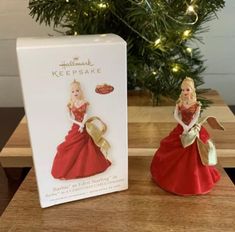 a christmas ornament with a red dress and gold bow on it next to a box