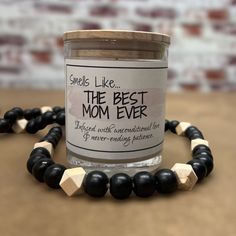 a candle that is sitting on top of a wooden beaded bracelet with the words smell like, the best mom ever