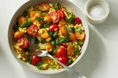 a bowl filled with corn and tomatoes next to a small bowl of salt on the side