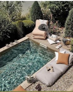 an outdoor swimming pool with chaise lounges and pillows on the ground next to it