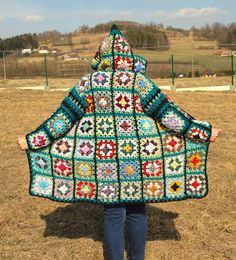 a woman is standing in the grass holding up a granny granny's afghan shawl