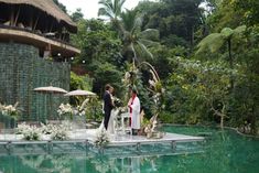 a bride and groom are standing on the edge of a pool at their wedding ceremony