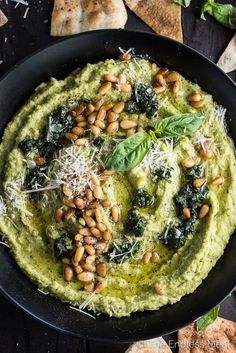 spinach dip with pine nuts and parmesan cheese in a black bowl surrounded by pita chips