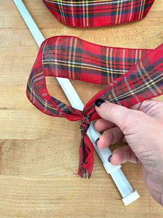 a hand is pulling the ribbon off of a red plaid bag