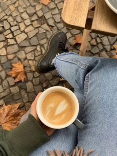 a person holding a cup of coffee while sitting on a bench with their legs crossed