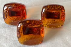 three orange glass cubes sitting on top of a white cloth covered table next to each other