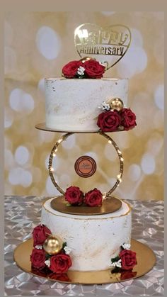 a three tiered white cake with red roses on the bottom and gold decorations at the top