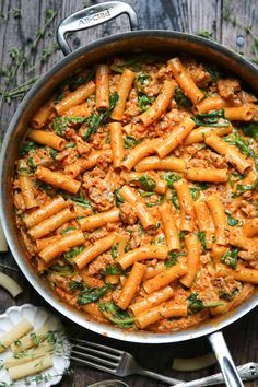 pasta with meat and spinach in a pan on a wooden table next to utensils