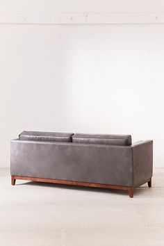 a gray leather couch sitting on top of a hard wood floor next to a white wall