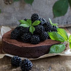 a chocolate cake topped with blackberries and mint leaves on top of a wooden table