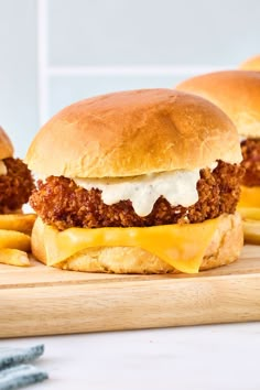 three sloppy joes with cheese and fries on a wooden cutting board next to them