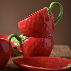 three red ceramic strawberry cups and saucers on a wooden table