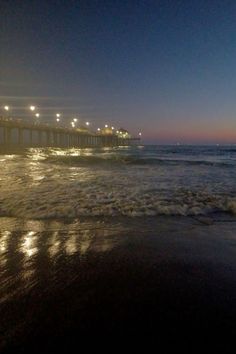 the pier is lit up at night on the beach