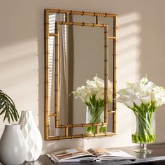 two vases with white flowers sit on a table next to a mirror and lamp