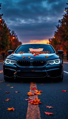 a blue car parked on the side of a road with autumn leaves all over it