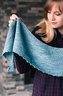 a woman holding up a blue knitted shawl