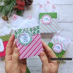 someone holding up some christmas gift bags on top of a wooden table with pine cones